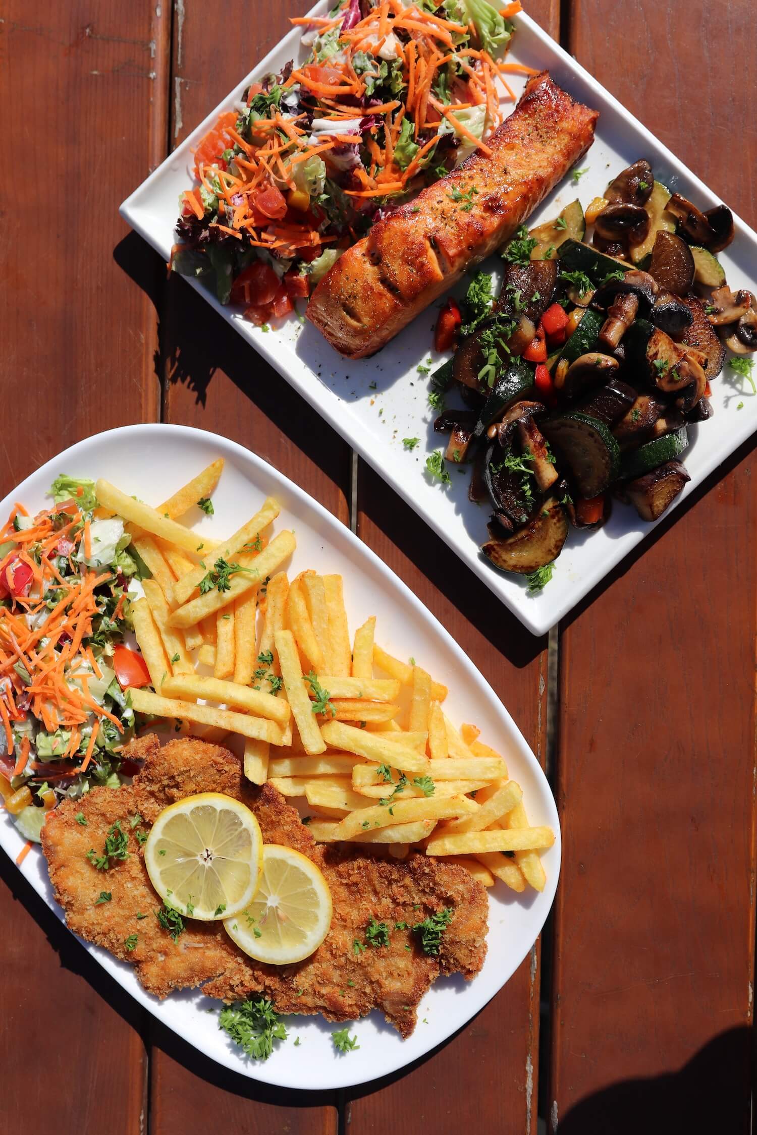 Zwei Gerichte auf Tellern: Schnitzel mit Pommes und gebratnere Lachs mit Gemüse im Schiffercafé Kiel